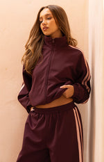 Burgundy track jacket with high collar, full zip front, pink sleeve stripes, and elasticated hem