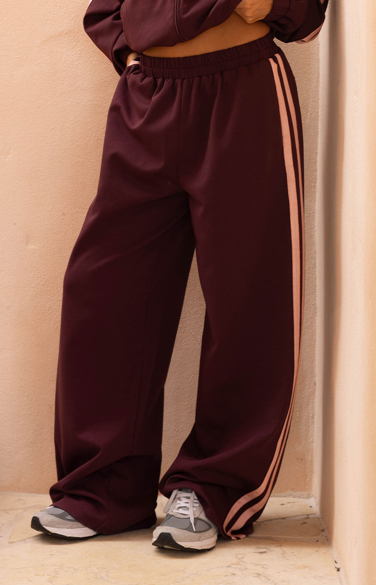 Close up of burgundy wide leg track pants with light pink side stripes comfortable for lounging or travel