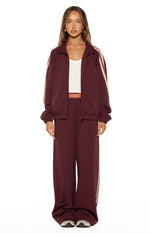 Front view of a relaxed fit burgundy track jacket with pink sleeve stripes, high collar, full zip, and elasticated hem
