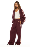 Close up of burgundy wide leg track pants with light pink side stripes comfortable for lounging or travel