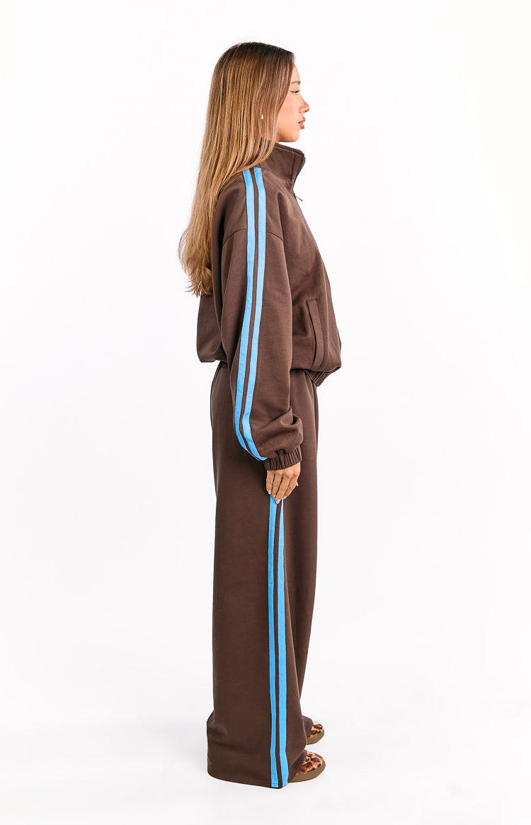 Side view of chocolate brown wide-leg track pants with a blue stripe down the side