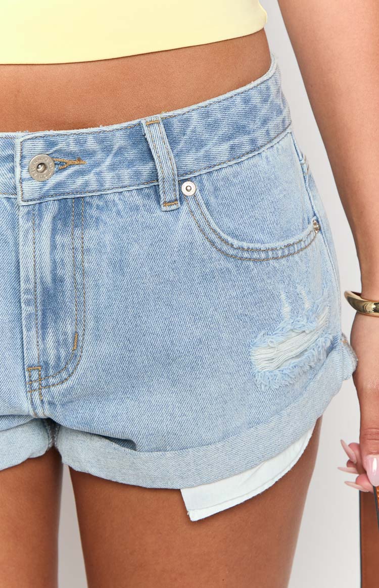 Close-up of the distressed rips and rolled cuffs on light wash denim shorts