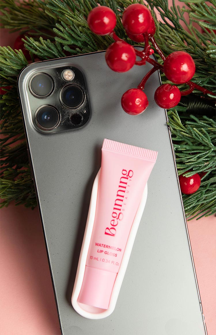 Pink lip gloss tube with 'Watermelon Lip Gloss' text in a white phone holder on a grey smartphone