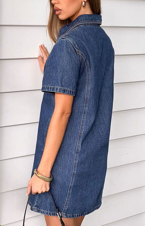 Side view of a dark wash denim mini dress showing the short sleeves, collar, and side seam stitching