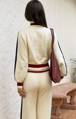 Rear view of a cream knit sweater with navy sleeve stripes, maroon trim on collar, cuffs, and double-striped hem, with matchi
