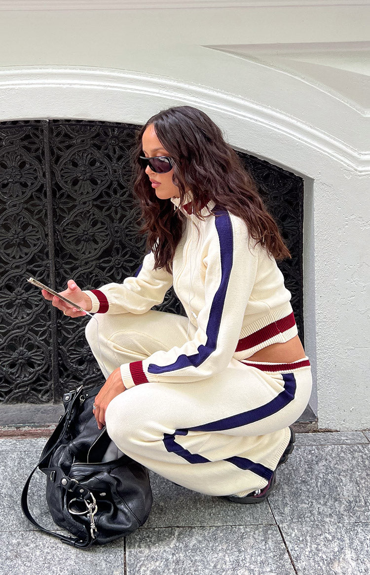 Side view of a cream knit zip sweater with cable jacquard texture, navy and burgundy sleeve stripes, and a cropped hem