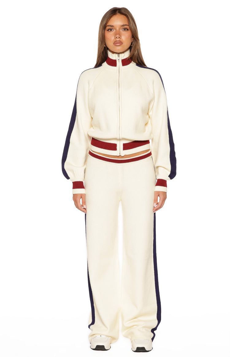 Front view of a cream knit zip sweater with a high red and cream ribbed collar, full zip, navy stripe long sleeves, and striped ribbed hem