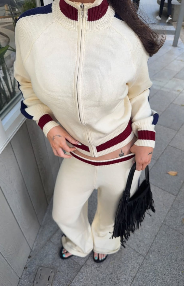 Cream knit zip sweater with burgundy and navy striped collar, cuffs, and hem, paired with matching wide-leg pants with a burg