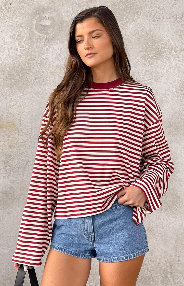 Wine red and white horizontal striped long-sleeve top with a wine red crew neck, paired with blue denim shorts. A black shoulder bag is held.