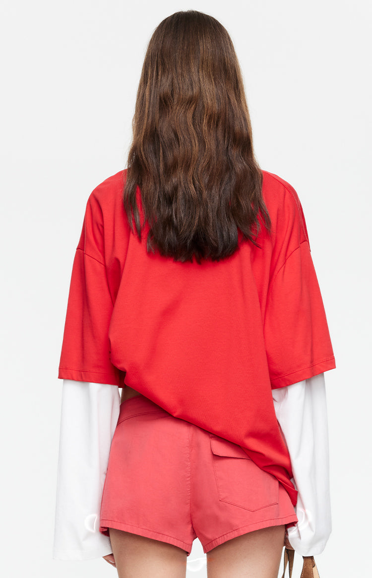 Rear view of the crimson red oversized short-sleeve shirt layered over a white long-sleeve shirt with wide cuffs