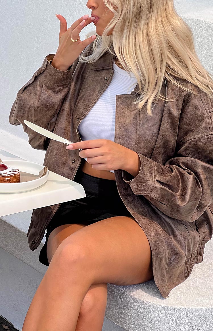 Close-up of the distressed chocolate brown bomber jacket with a collared neckline and textured faux leather