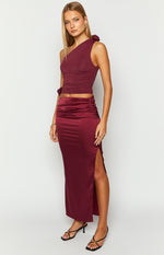 Front view of a burgundy satin maxi skirt with a high side slit and ruched detail at the waist