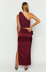 Rear view of a burgundy satin maxi skirt with a high side slit and ruched rose detail on the hip