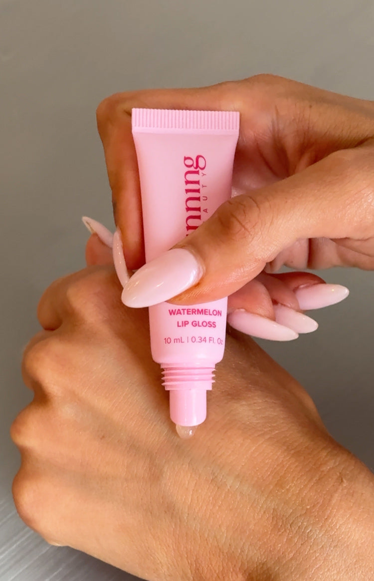 A clear, shiny drop of lip gloss being dispensed from the applicator tip of a light pink tube