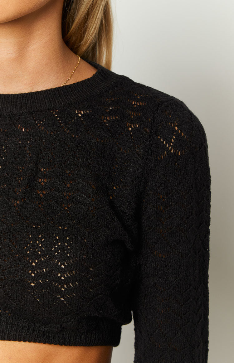Close-up of the black knit top showing the intricate open-knit pattern and ribbed crew neck