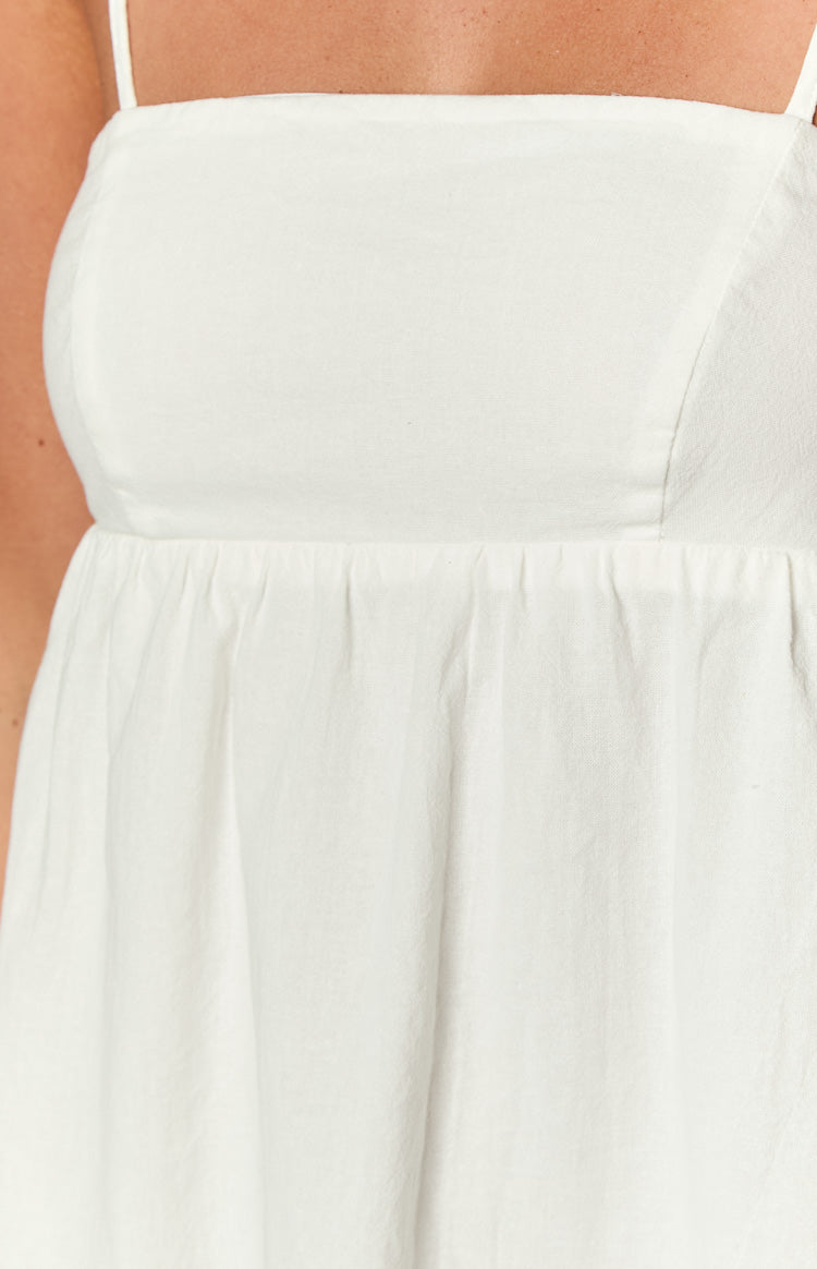 Close-up of the white mini dress showing the square neckline, thin spaghetti straps, fitted bodice, and gathered waist in textured fabric