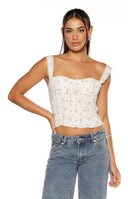 Our model wears a fitted bustier-style crop top in a light-colored fabric with a delicate all-over floral print of small purple and yellow blossoms. The top features a sweetheart neckline a ruched or shirred texture through the bodice and wide lace-trimmed shoulder straps. The shirt ends just above the navel.