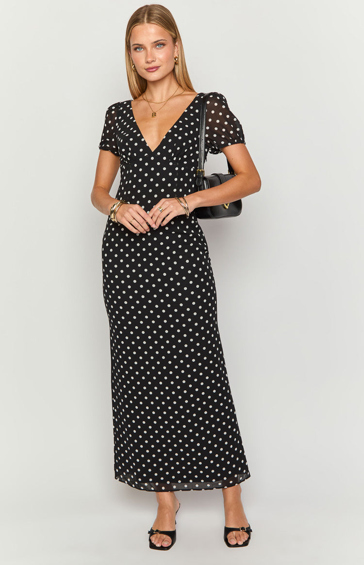 Front view of a black polka dot maxi dress with a V-neck, short sheer puff sleeves, and a flowing skirt