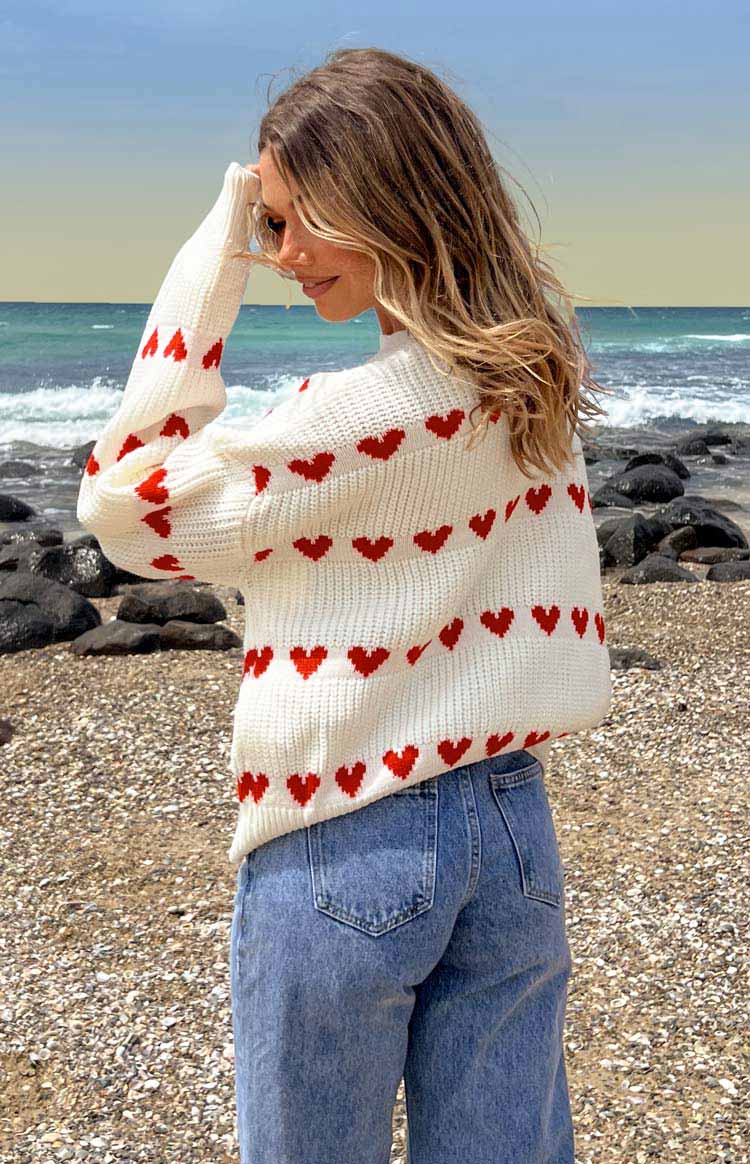 Rear view of a white knitted jumper with red heart patterns in horizontal stripes and ribbed cuffs