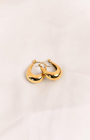 A pair of thick, polished gold-toned hoop earrings with a smooth, teardrop-like shape.