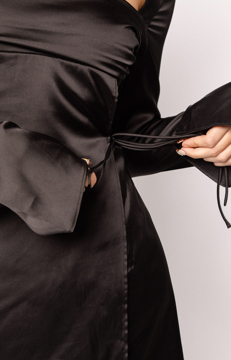 Close-up of the adjustable side tie detail on a black satin mini dress with wide cuffs