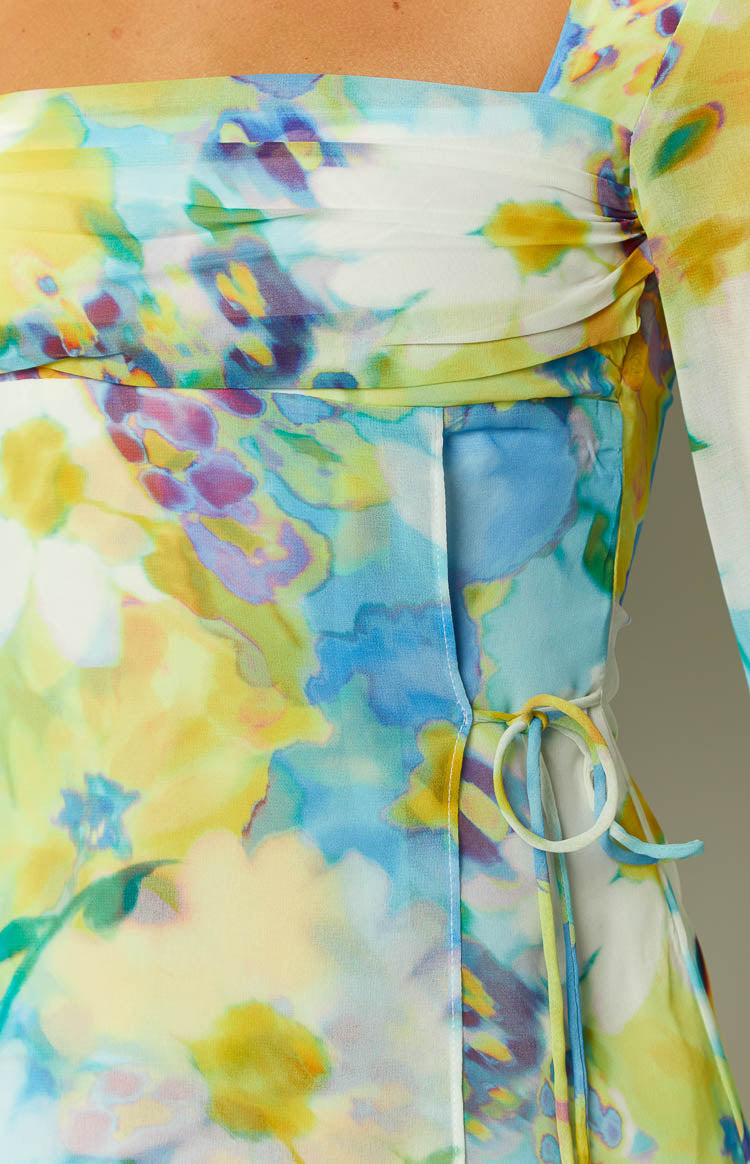 Close-up of the ruched bust, side seam, and waist tie detail with white rings on a blue and yellow floral dress