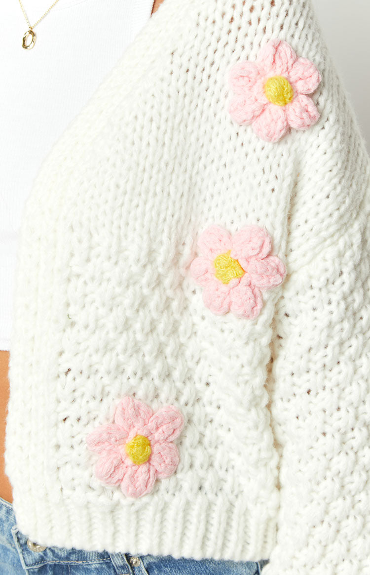 Close-up of the chunky white knit cardigan with pink knitted flower appliques and yellow centers