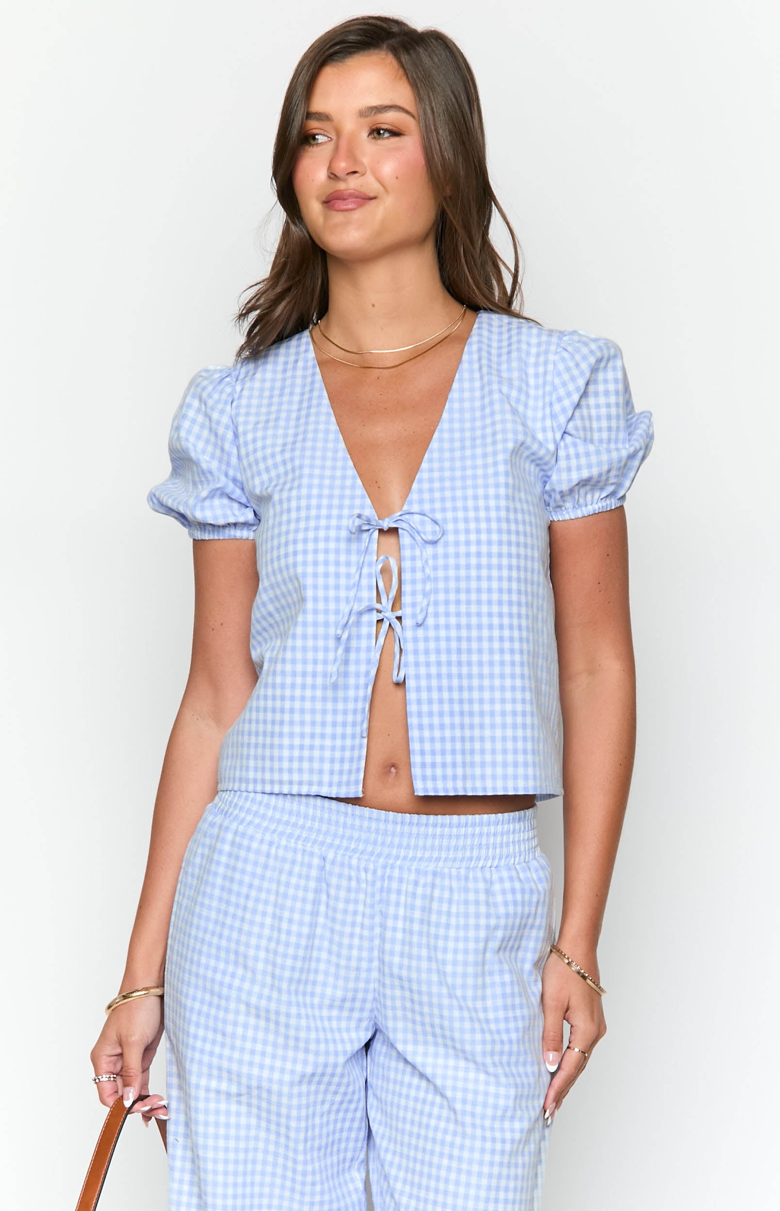 Front view of a blue gingham tie-up top with a deep V-neck and short puffed sleeves
