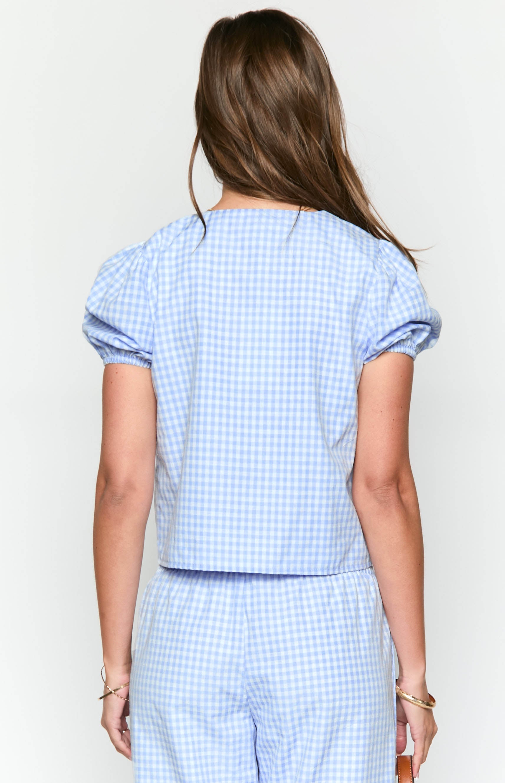 Rear view of a blue gingham top with short puff sleeves and elasticated cuffs