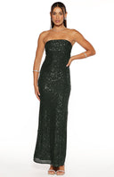 Our model wearing a strapless maxi gown in a shimmering emerald green color. This entire maxi is covered in vertical lines of fine glistening sequins giving it a sparkling texture and a straight column silhouette. A reflection in the mirror shows a cut-out detail on the back of the maxi dress.