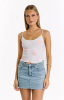 A close-up of a white spaghetti strap top adorned with pink and yellow beaded hibiscus flowers- paired with a light wash denim mini skirt.