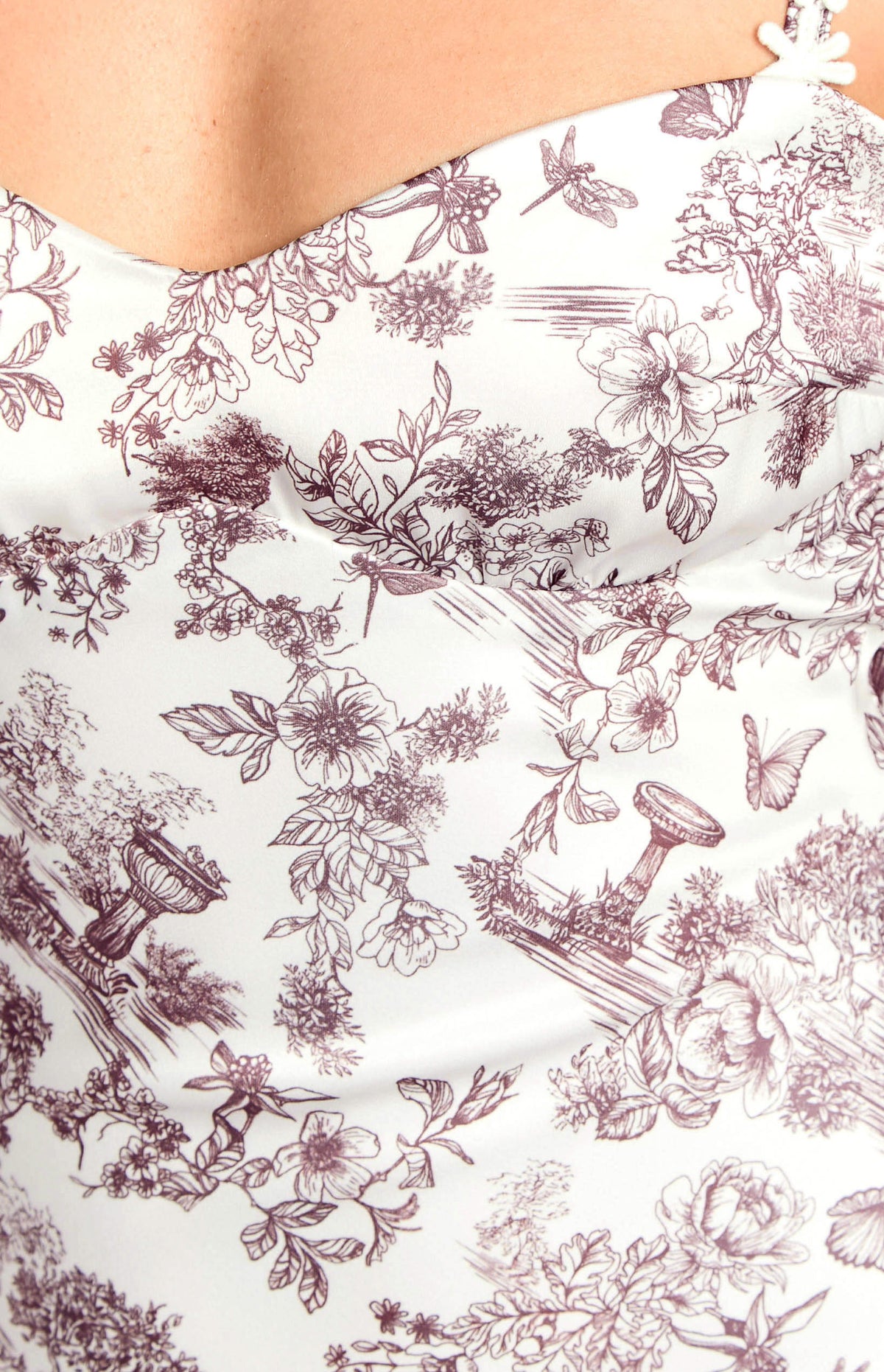 Close-up of the white satin fabric with a brown toile garden print featuring flowers, butterflies, and watering cans