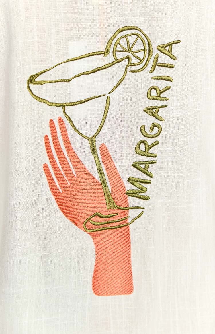 Close-up of the embroidered coral hand holding a green margarita glass and MARGARITA text on a white long sleeve shirt