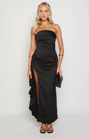 blonde model wearing black maxi dress with side ruffle, with black heels and black bag