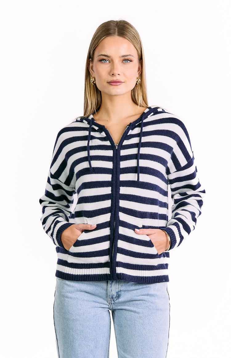 Front view of a navy and white striped knit zip sweater with a hood, drawstrings, and hands in the front pockets