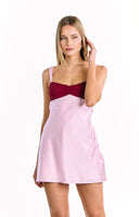A feminine color-blocked mini-dress with a dark red bust featuring a twisted detail and a light pink satin-like skirt. Our dress has wide pink shoulder straps.