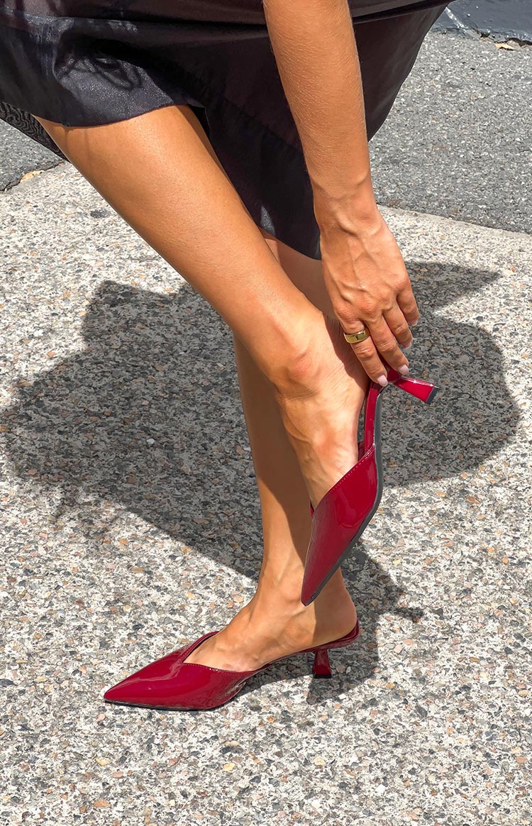 Side profile of a cherry red patent mule heel, showing the pointed toe and low kitten heel