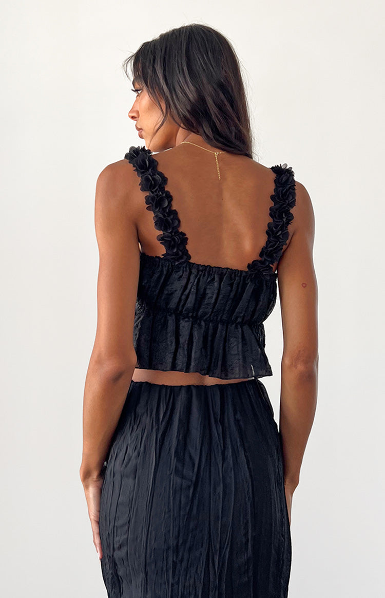 Rear view of a black top with floral applique straps and a shirred back with a ruffled hem