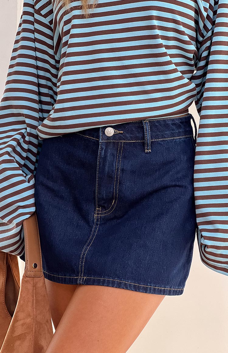 Front close-up of a dark denim mini skirt, showing the silver button, belt loops, and light brown contrast stitching