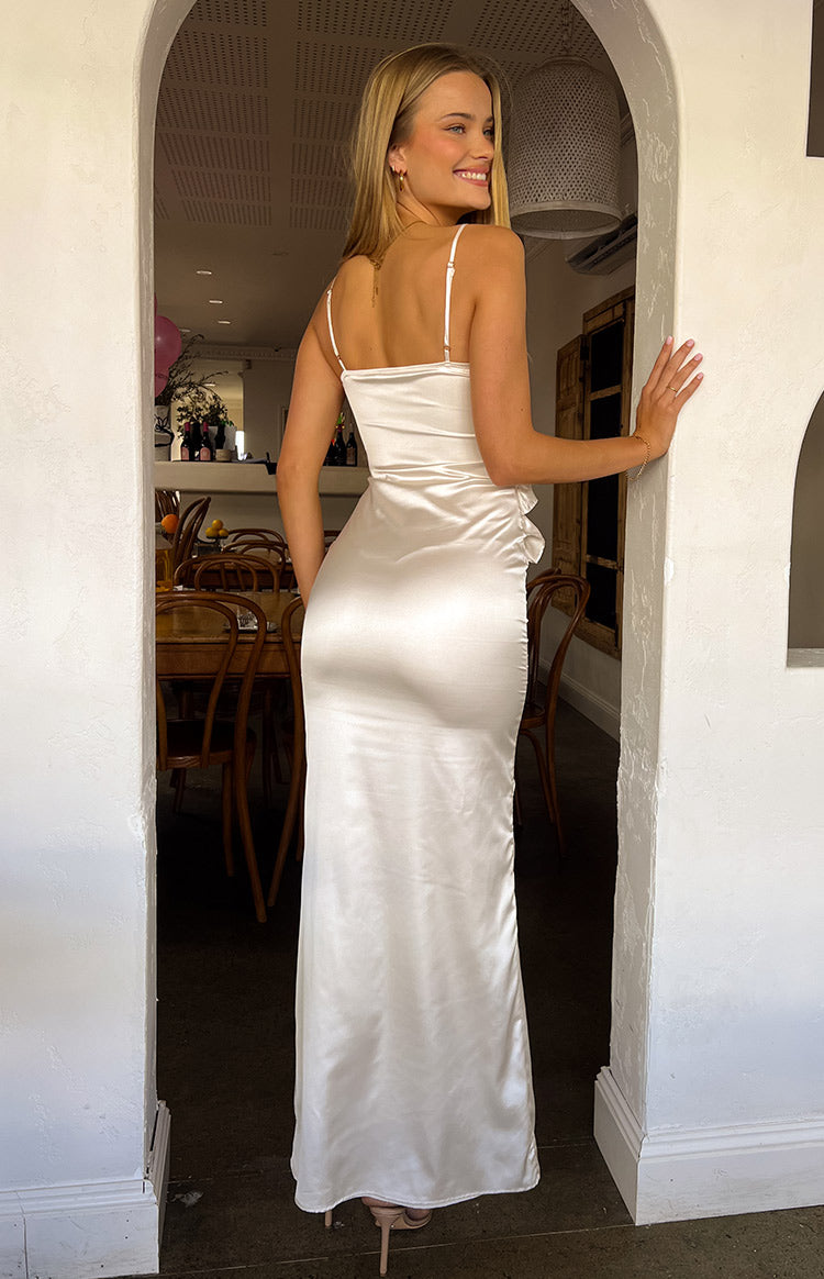 Rear view of a cream satin maxi dress with thin spaghetti straps and a fitted skirt featuring a side ruffle