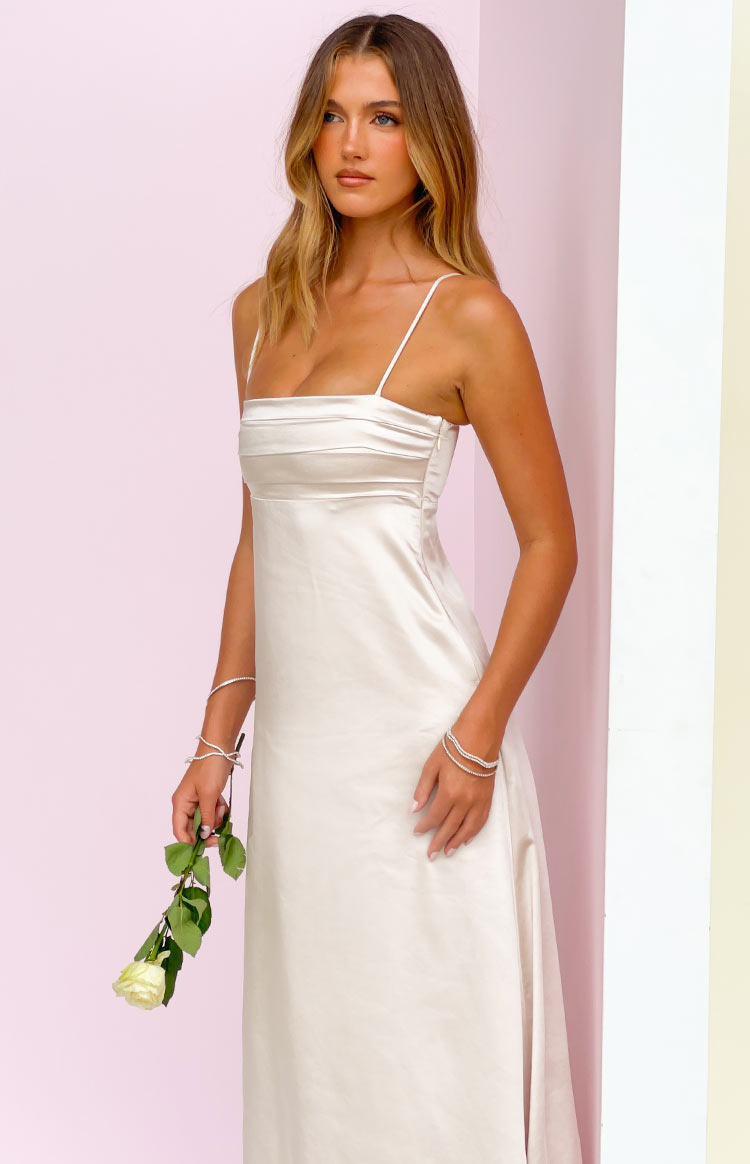Side view of a cream satin maxi dress with a square neckline, thin spaghetti straps, pleated bust, and side zipper