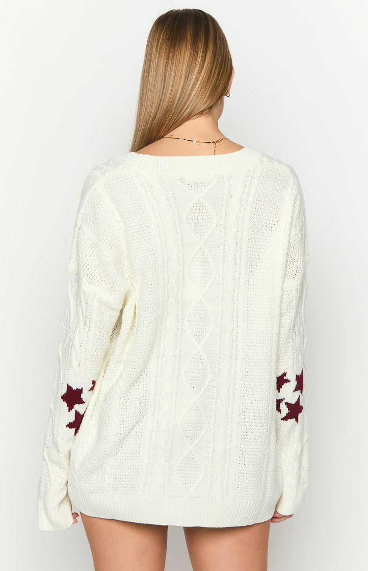 Back view of an oversized white cable knit cardigan with a round neck and maroon star patterns on the sleeves