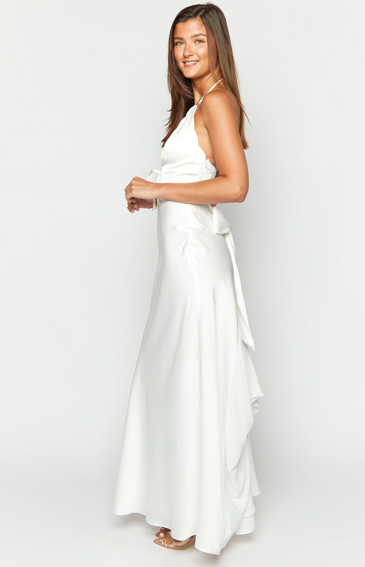 Side view of a white halter neck maxi dress with a front tie detail and a long back tie creating a flowing drape
