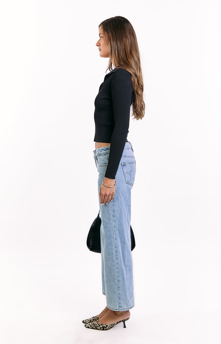 Side view of the black ribbed knit long sleeve sweater, showing its collared neckline and cropped hem