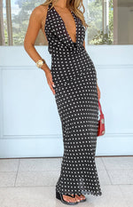 Full length view of a black polka dot maxi dress with a deep cowl halter neck and flowing skirt