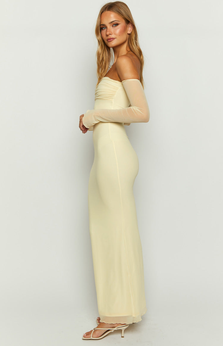 Side view of a cream off-shoulder ruched maxi dress with sheer long sleeves and a fitted silhouette