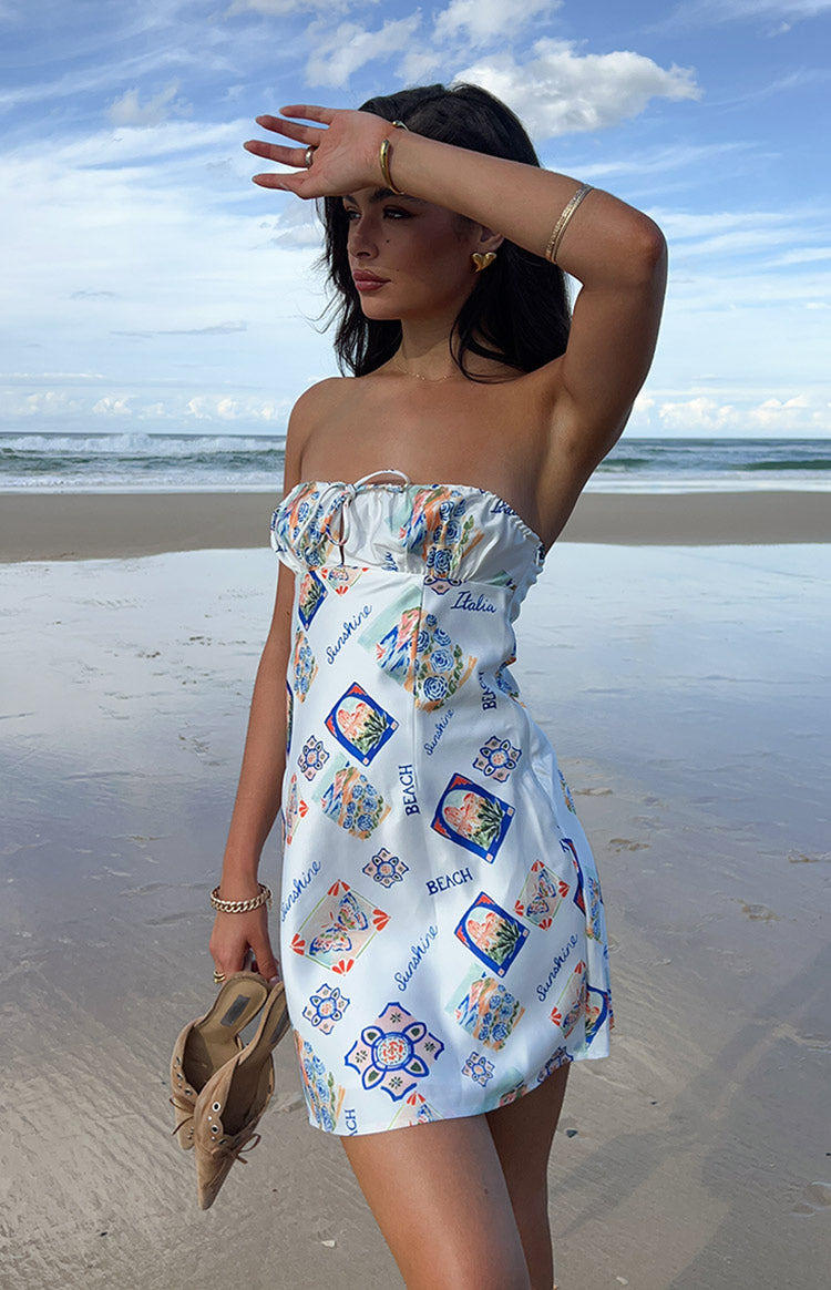 Side view of a white strapless mini dress with a drawstring bust and blue and orange Italia print