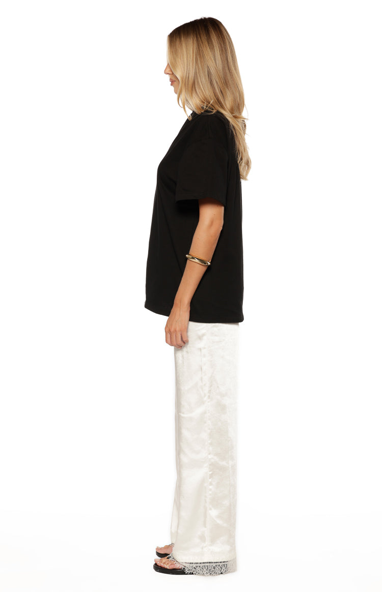 Side view of ivory satin straight leg pants with a smooth drape and delicate lace trim at the hem
