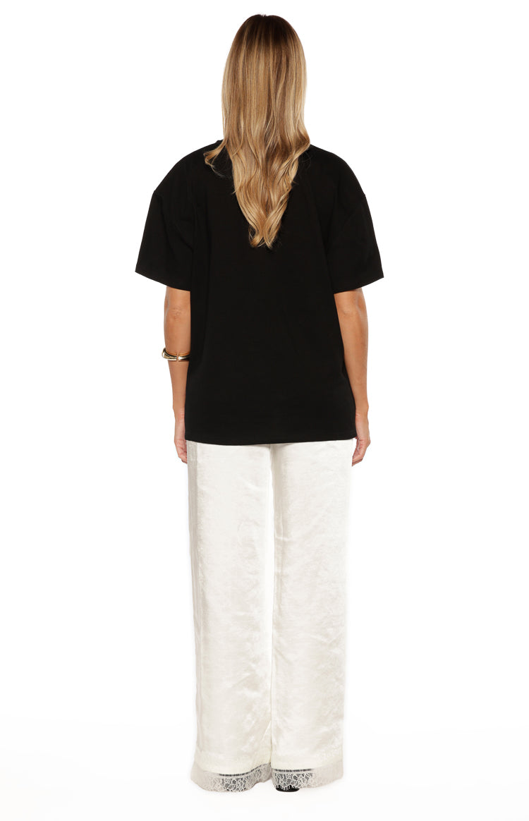 Rear view of ivory satin straight leg pants with delicate lace trim at the hem