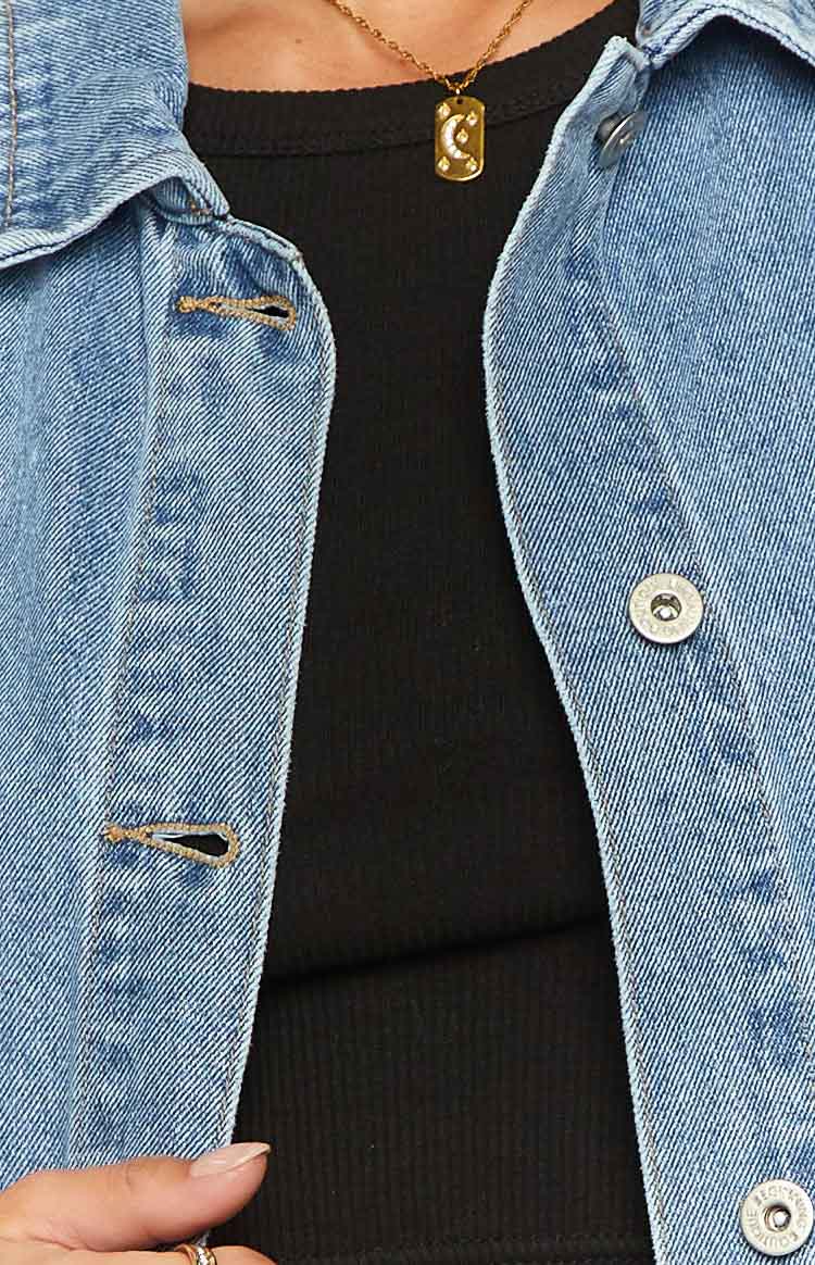 Close-up of the mid-wash denim vest's front placket with a silver button and buttonhole detail